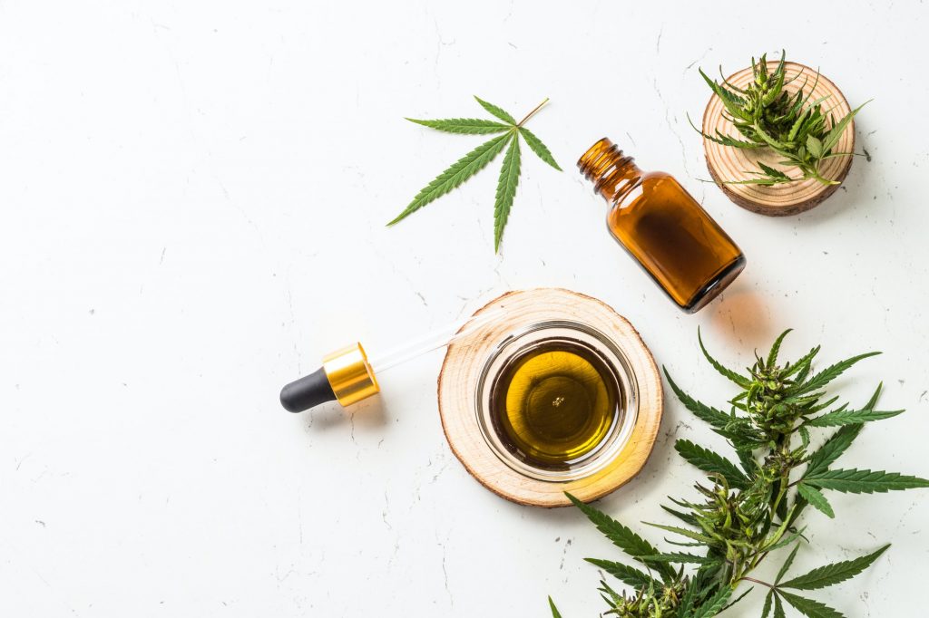 CBD oil and cannabis leaves at white table